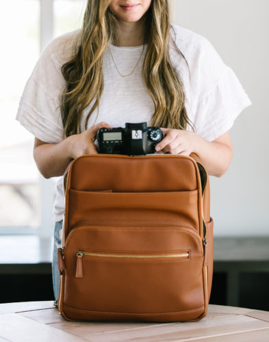 woman holding camera on top of travel bag