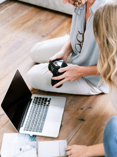 Two women sitting on the floor with a laptop and camera lens